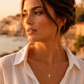 Collier petite croix plate en or jaune 18 carats massif porté de profil par une femme au coucher du soleil.
