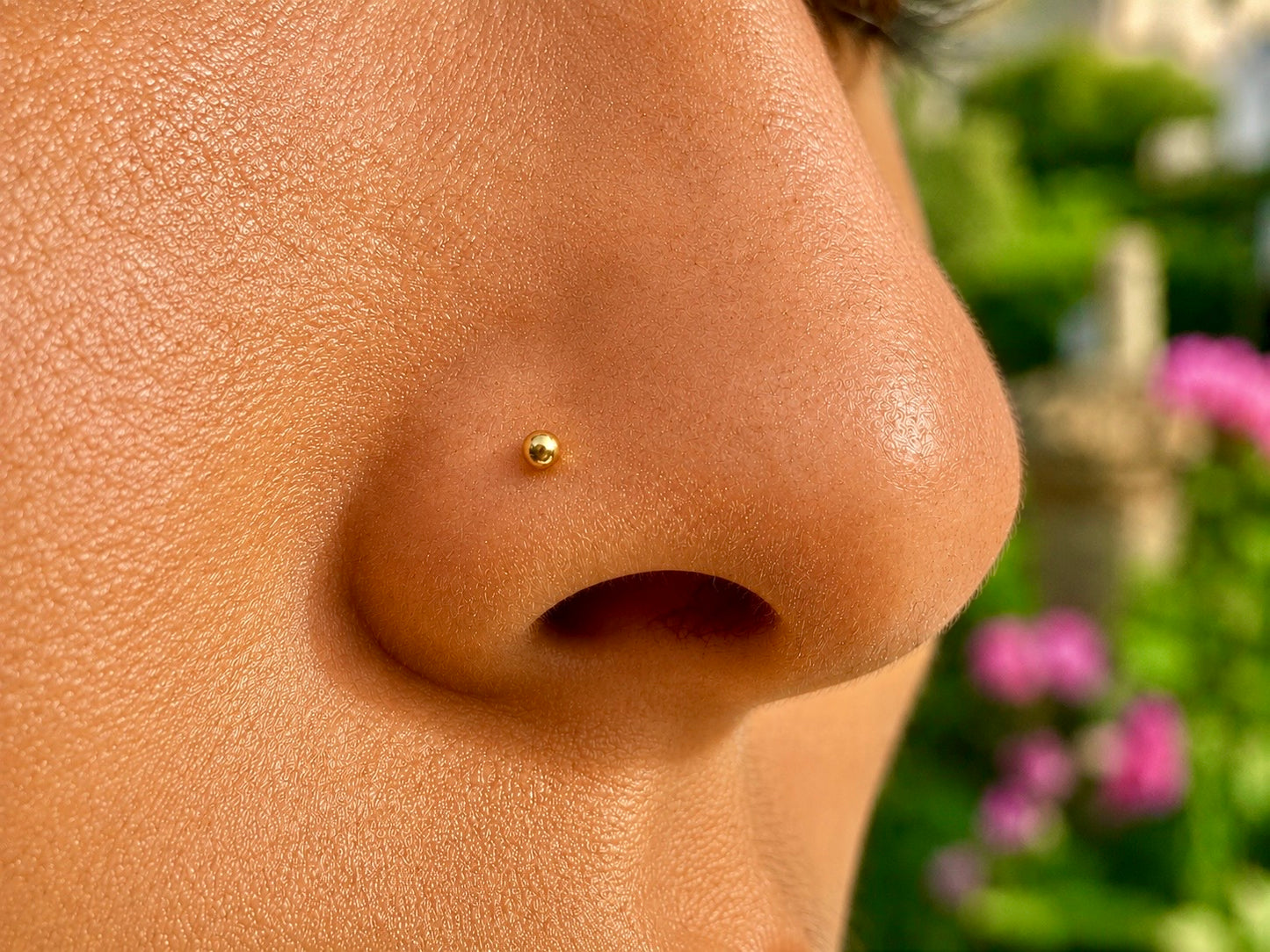 Gros plan sur la narine d'une personne portant un piercing nez boule en or jaune 18 carats, un bijou de nez discret et élégant de l'atelier La Fille du Sud.