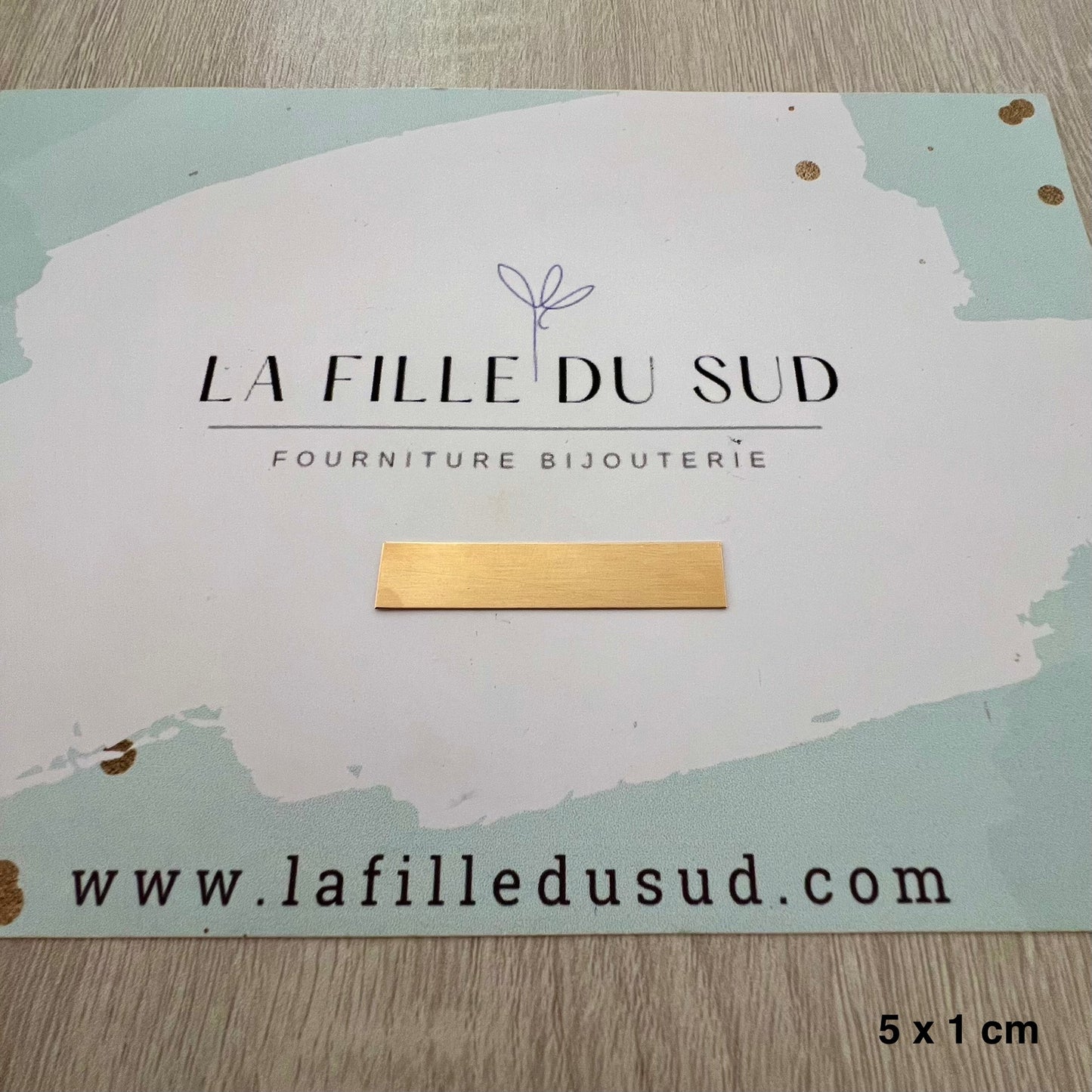 Plaque en or jaune 18 carats de 5 cm par 1 cm présentée sur la carte de l'atelier La Fille du Sud.