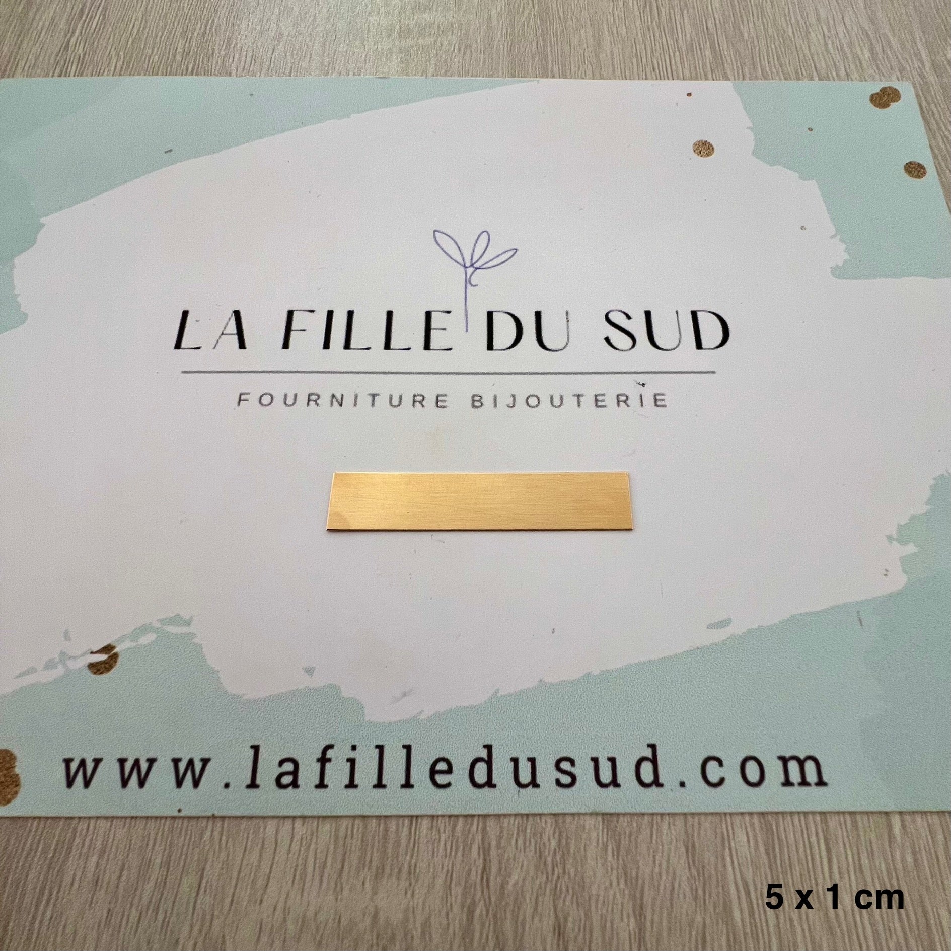 Plaque en or jaune 18 carats de 5 cm par 1 cm présentée sur la carte de l'atelier La Fille du Sud.