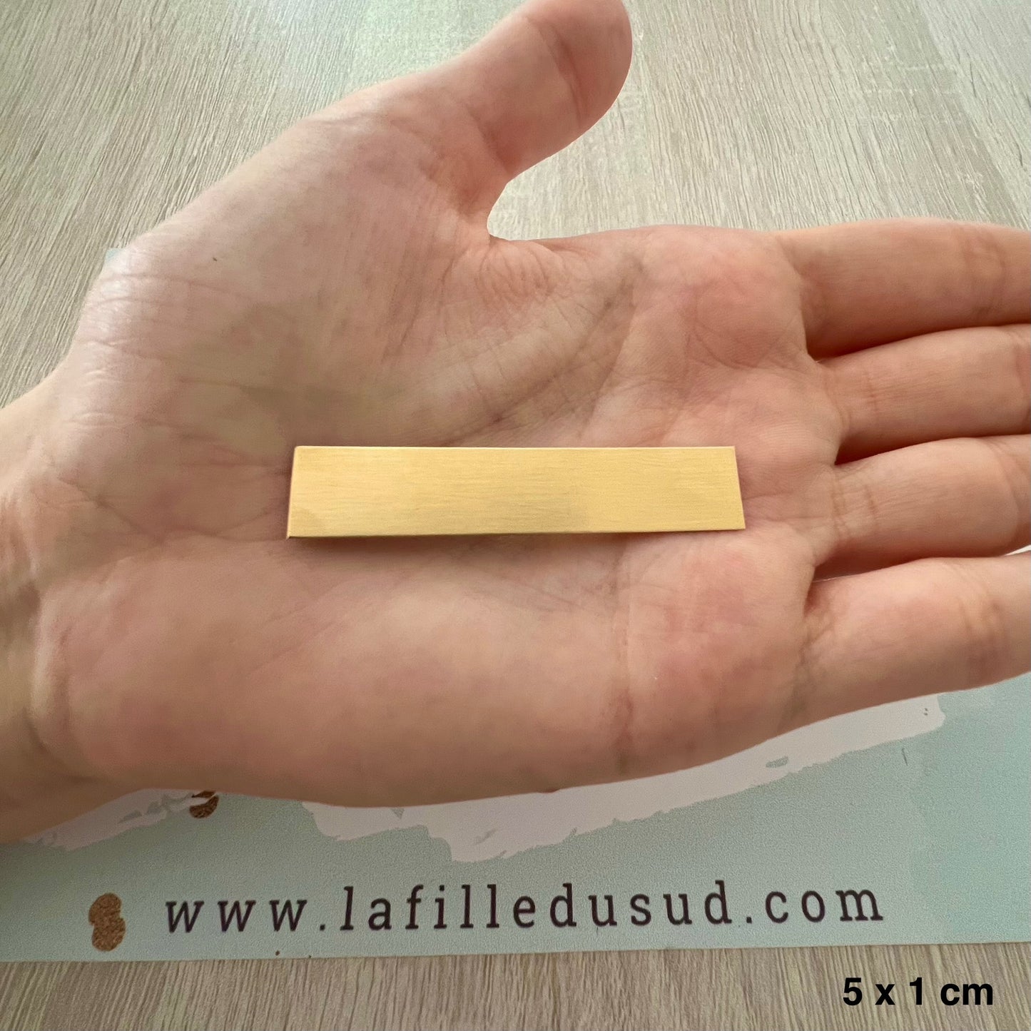 Aperçu de la taille réelle de la plaque d'or de 5x1 cm dans la paume de la main d'un créateur.