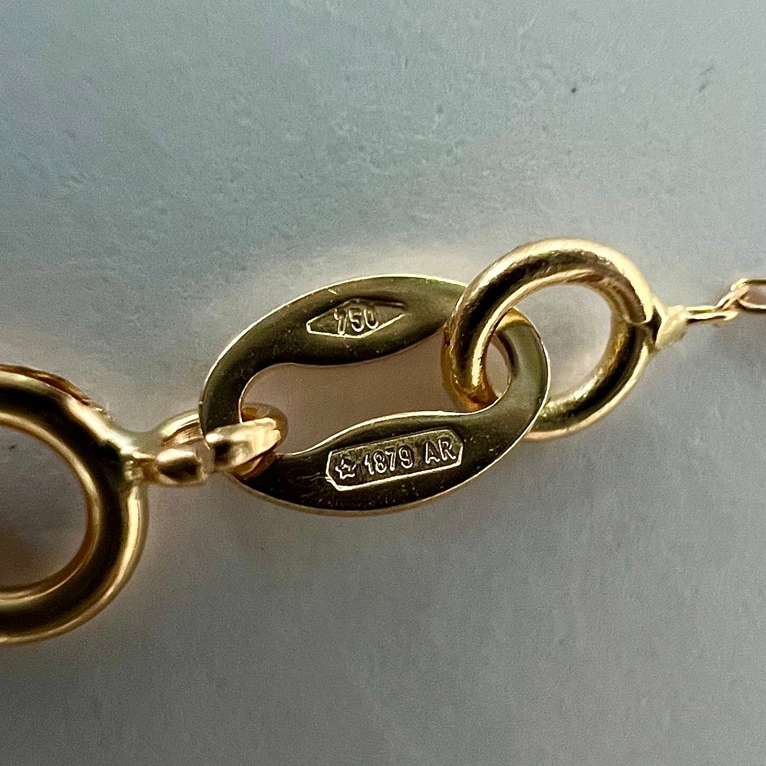 Gros plan sur le poinçon d'état 750 garantissant l'authenticité de l'or 18 carats massif du collier boule solitaire.