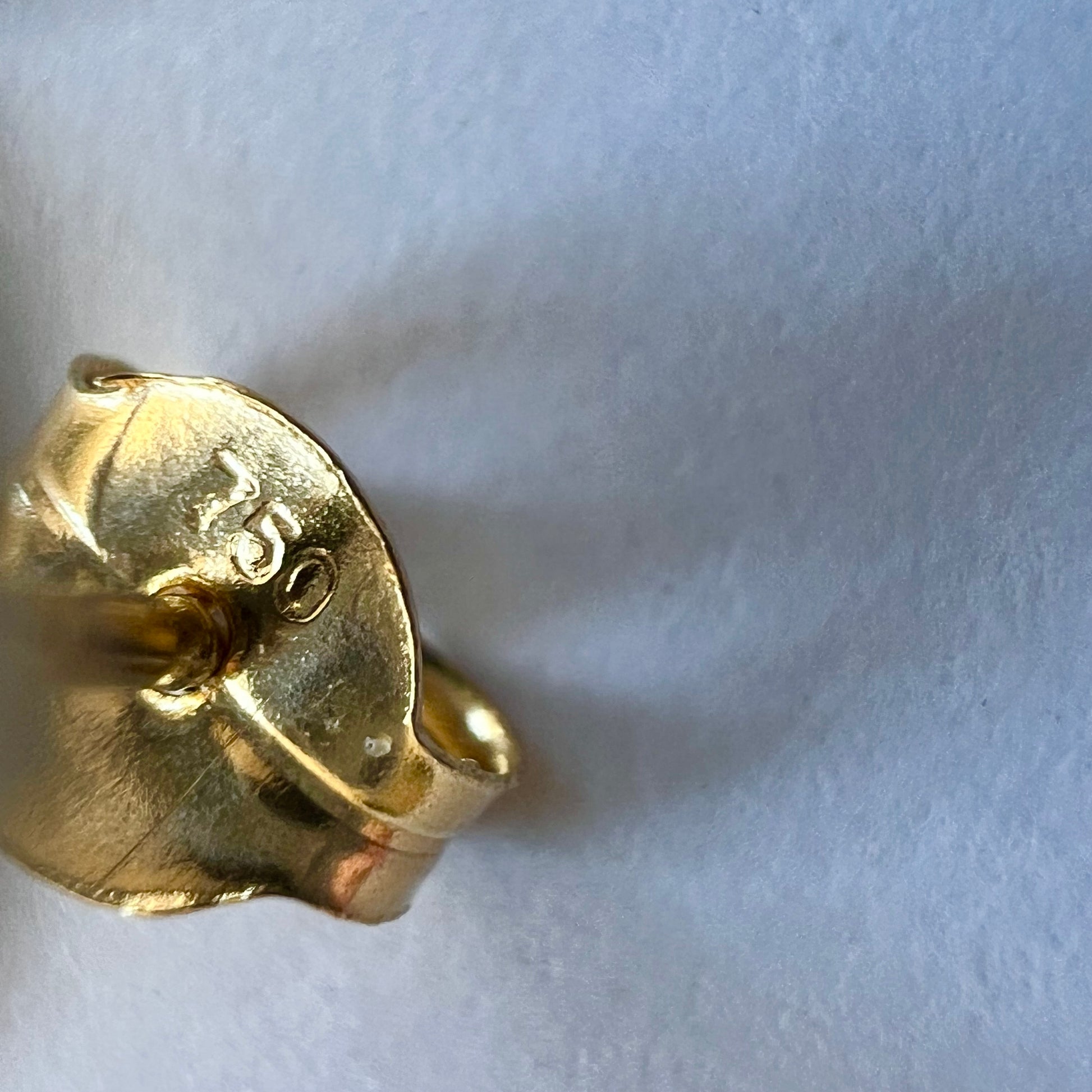 Zoom sur le poinçon d'état 750 garantissant l'authenticité de l'or 18 carats massif du fermoir papillon de la boucle d'oreille demi-sphere