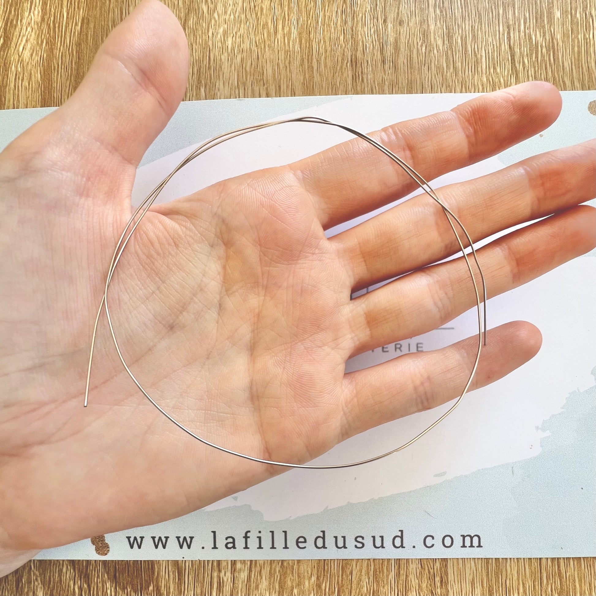 Proportion d'un fil d'or gris 18 carats pour artisan bijoutier tenu en grande boucle dans la main.