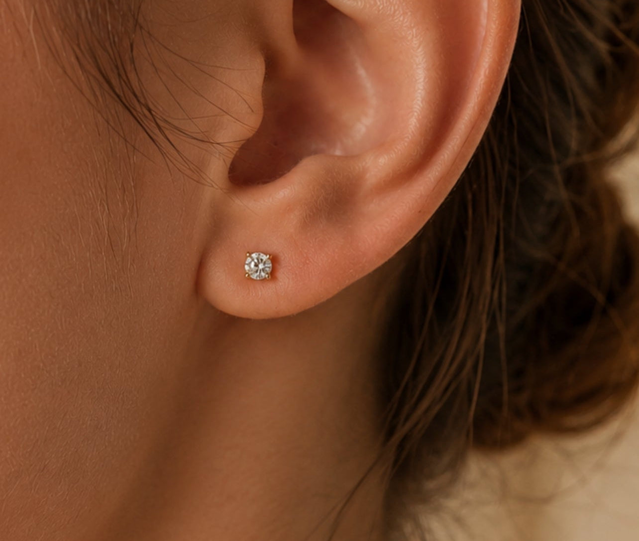 Gros plan sur une oreille de femme portant une puce d'oreille en diamant solitaire et or jaune 18 carats, éclat naturel et élégance minimaliste.
