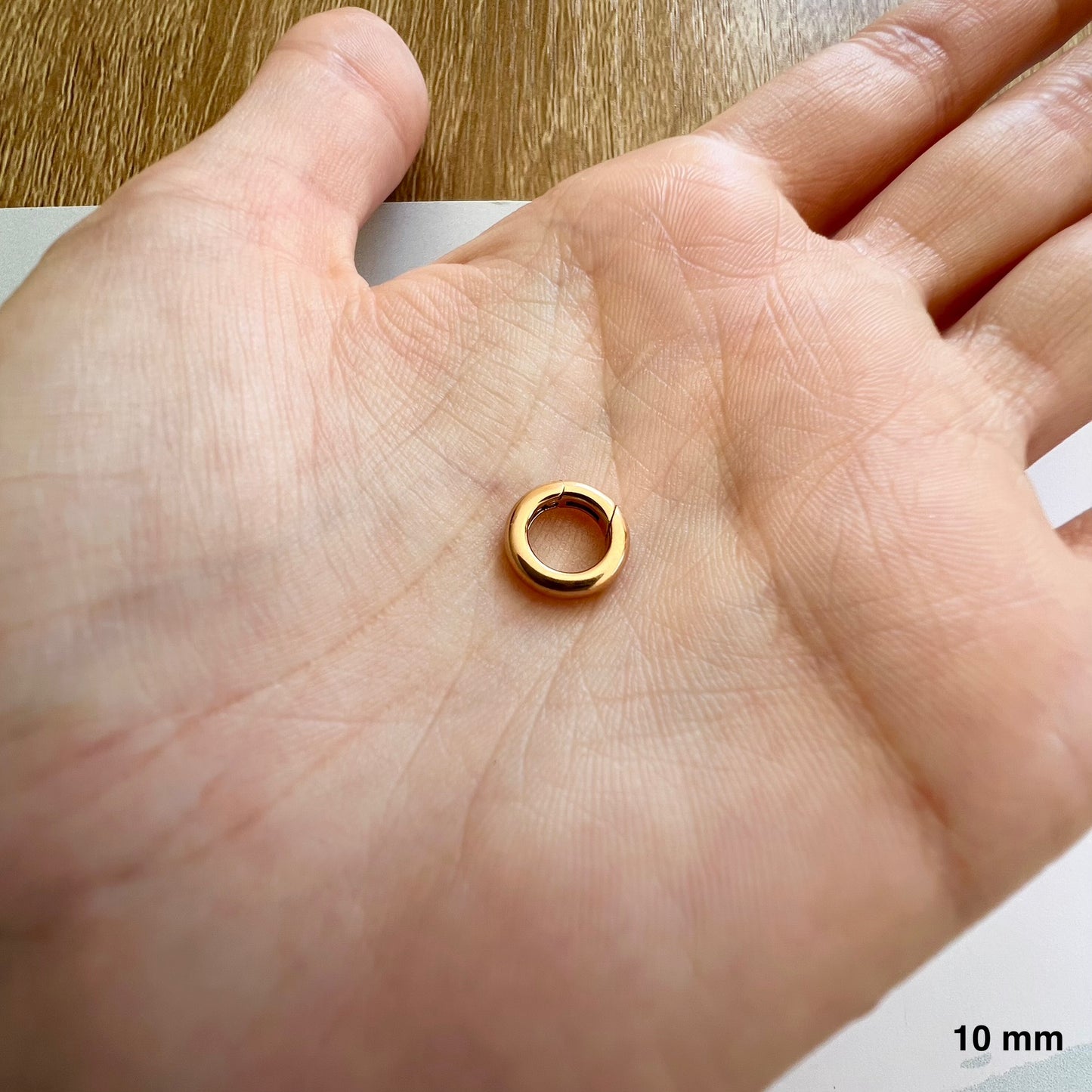 Taille réelle d'un fermoir à charnière invisible de 10 mm en or rouge 18 carats dans la paume d'une main.